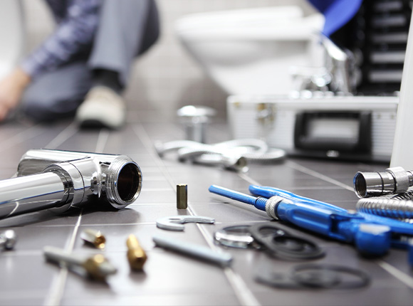 plumbing tools and fixtures scattered on a floor with a person working in the background 11 essential repair items in focus