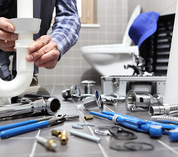 plumber working on pipe installation surrounded by tools toilet in background 9 essential tools for plumbing repairs