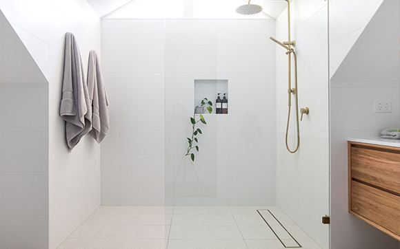 modern bathroom shower with glass enclosure featuring white tiles gray towels and a wooden vanity three simple beauty products displayed inside the glass wall