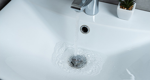 water flowing from a modern faucet into a sleek sink with ripples forming around the drain suitable for a 16 inch basin with a small plant in the background