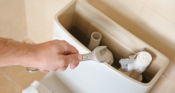 hand holding a wrench above toilet tank plumbing repair tools and components related to 12 essential maintenance tips