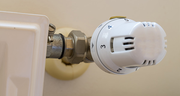 thermostat attached to a radiator valve with numbered settings for temperature control in an 18 degree heating system