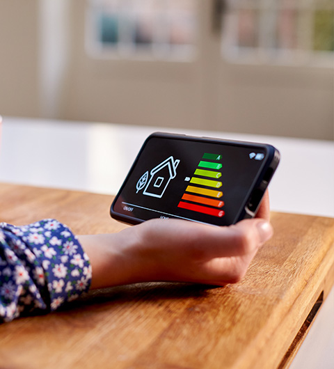 hand holding smartphone displaying home energy efficiency levels with green yellow and red indicators for energy saving options and tips five energy levels