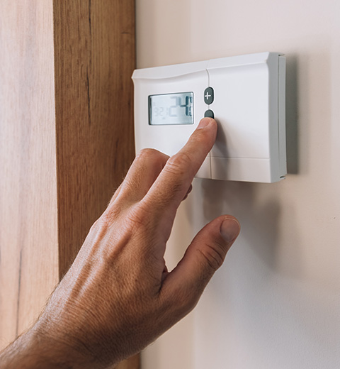hand adjusting a digital thermostat displaying temperature settings for efficient home heating and cooling control