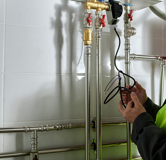 a technician inspecting plumbing pipes and wiring in a maintenance environment focusing on tools and safety equipment for plumbing systems