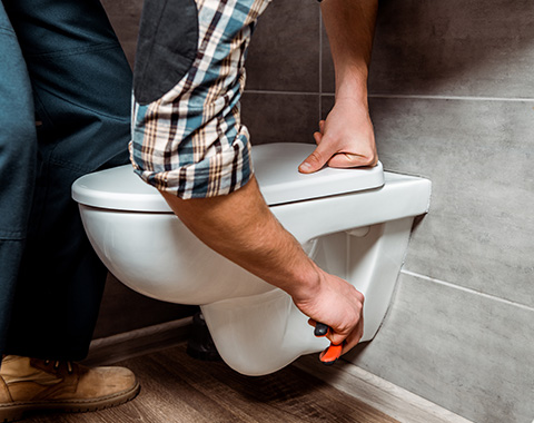 person installing a toilet in a bathroom with a checkered shirt focused on plumbing repair tools used for the toilet installation process