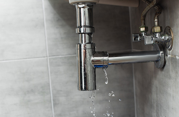 leaking chrome sink drain pipe with water droplets in a modern bathroom highlighting importance of plumbing repairs 5 tips for homeowners