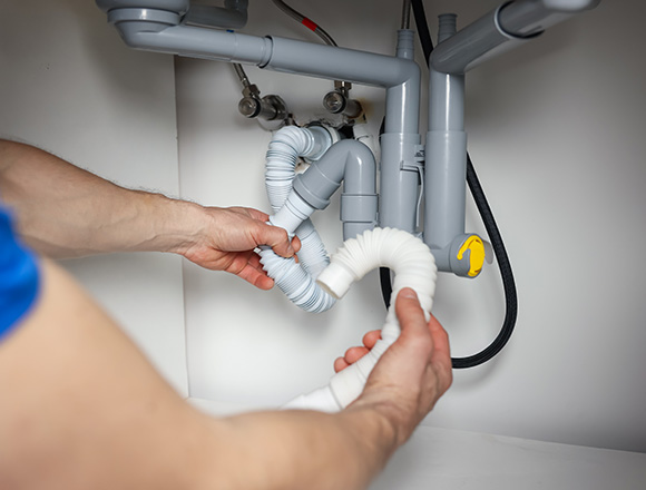 person working on plumbing under sink adjusting pipes and hoses fixing drain issues