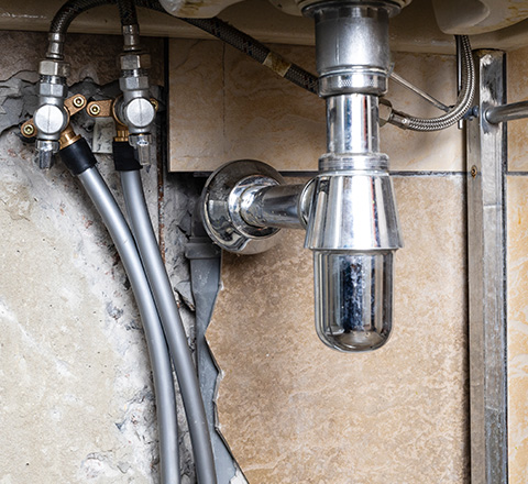 chrome plumbing fixture under a sink with visible pipes and wall damage suitable for home improvements 4 plumbing tips